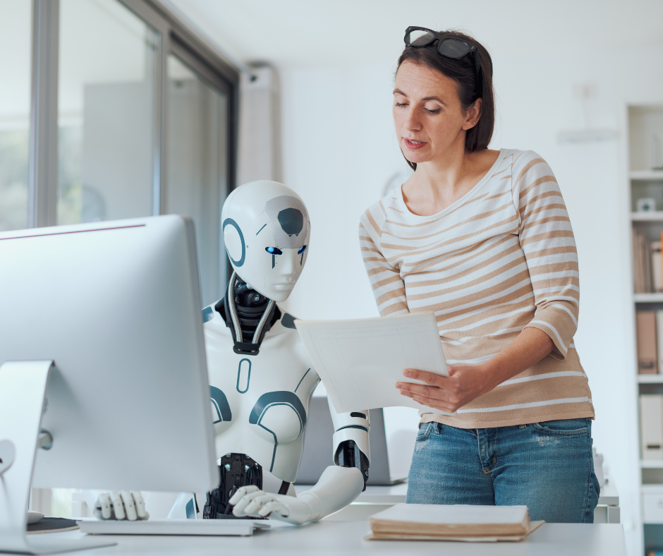 Kobieta pokazująca dokumenty robotowi AI siedzącemu przy komputerze podczas pracy nad wnioskiem o dotację