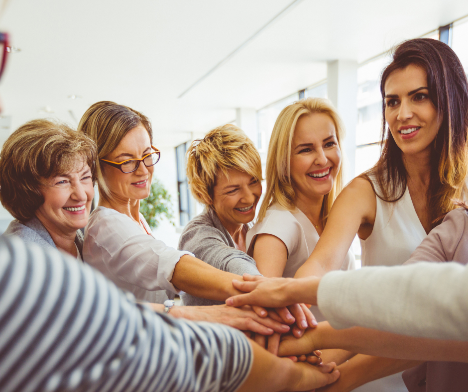 Kobiety w różnym wieku układają dłonie jedna na drugiej, symbolizując networking, współpracę i wzajemne wsparcie w biznesie